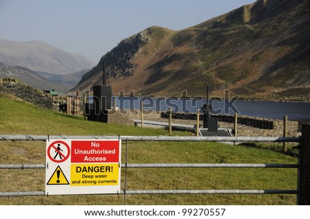 Warning sign on a gate saying no unauthorised access and advising of deep water and strong currents with Ennerdale lake in the English Lake District in the background