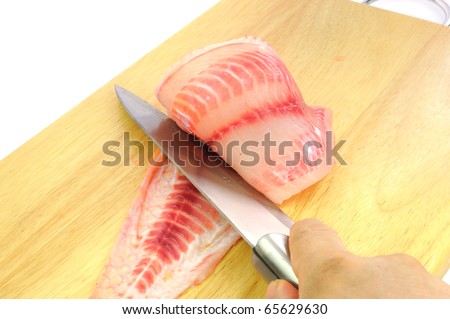 Knife on a hand slicing Red tilapia preparation for steak on wooden Cutting Board.