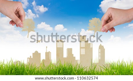 Woman hand put Paper cut of tree over  city and grass with blue sky