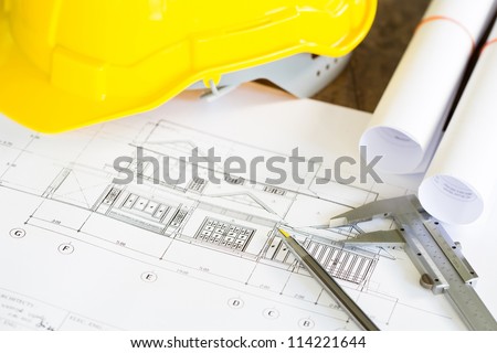 Construction plans with yellow helmet and drawing tools on blueprints