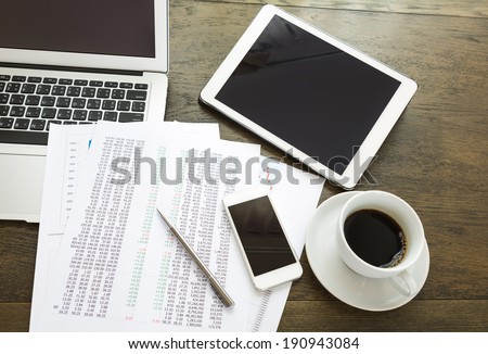 Laptop, tablet , smartphone and coffee cup with  financial documents on wooden table