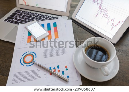 Laptop, tablet , smartphone and coffee cup with financial documents on wooden table