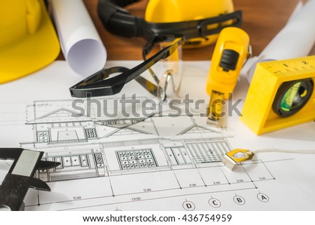 Construction plans with yellow helmet and drawing tools on blueprints