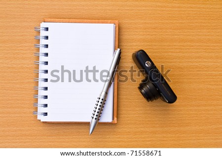Note book and pen and camera. On the floor of the wooden table.