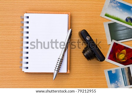 Note book , photo , pen and camera. On the floor of the wooden table.