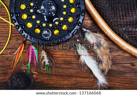A fly fishing reel with flies and a landing net on a wet wooden background