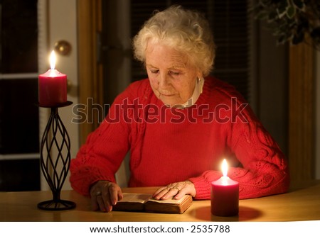 Elderly lady sitting in candlelight reading the bible during a power outage