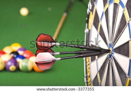 darts in a dart board with a pool game in the background(shallow dof)