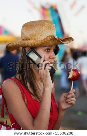 A beautiful young woman talking on a cell phone with a candy apple in hand