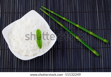 Bowl of steamed rice on a black place mat with bamboo chopsticks