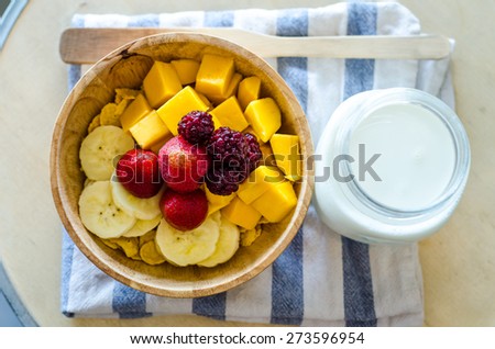 Variety of fresh fruit on corn flakes in a wooden bowl place beside a jug of fresh milk