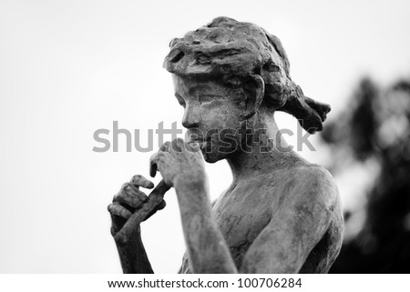 Old bronze statue of girl playing a flute. Black and white photo with shallow depth of field.