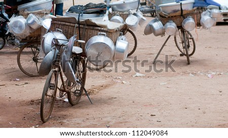 Pots and pans on bicycles belonging to vendors selling hardware in rural Cambodia. Shallow depth of field with the nearest bicycle in focus.