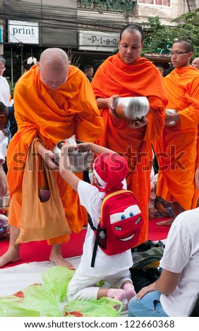BANGKOK - DECEMBER 23: Boy with a Santa Claus hat giving alms at a mass alms giving in celebration of the 2,600th anniversary of Lord Buddha\'s enlightenment on December 23, 2012 in Bangkok, Thailand.