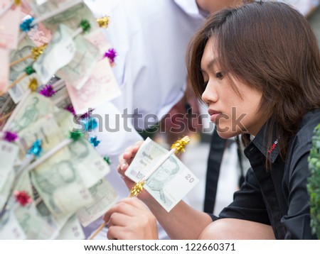 BANGKOK - DECEMBER 23: Woman giving alms, a 20 baht note during a mass alms giving in celebration of the 2,600th anniversary of Lord Buddha\'s enlightenment on December 23, 2012 in Bangkok, Thailand.