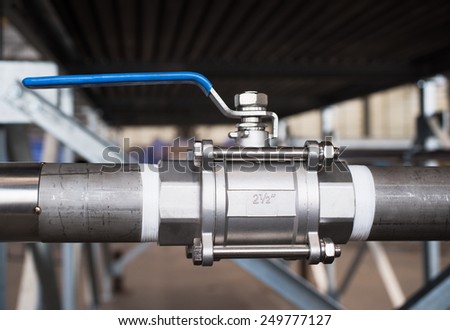 Stainless steel, 2.5 inch ball valve at an industrial workshop. Shallow depth of field with the valve in focus.