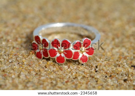 Silver ring with red enamel flowers on a wet beach. Shallow depth of field.