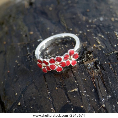 Silver ring with red enamel placed on a wet coconut on the beach. Grains of sand visible on the coco-nut. Shallow depth of field.