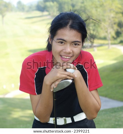 Young, female golf player smiling, holding golf club and ball, with fairway in the background.