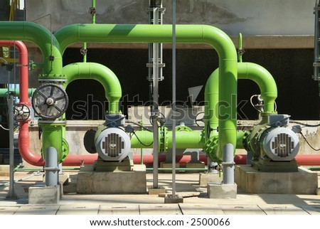 Pumps, valves and green steel pipes at industrial cooling tower.