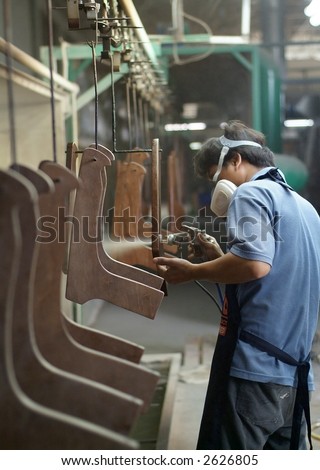 Factory worker spray painting furniture parts at an assembly line