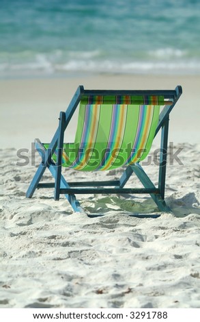 Green lawn chair on a sunny beach facing the ocean. Shallow depth of field with background out of focus.