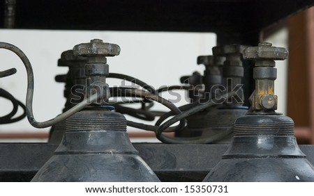 Battery of old gas bottle with only the tops and the valves of the bottles visible. Shallow depth of field with the nearest bottles in focus.