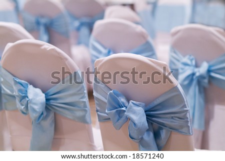 Chairs for a party with pink covers and sky blue ribbon and bow. Shallow depth of field with the first chair in focus