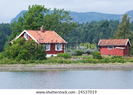 Two small, red, wooden, Scandinavian style houses by the sea.
