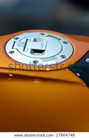 Gas cap of orange, large motorbike. Very shallow depth of field with focus around the center of the cap.