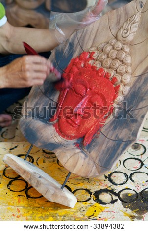 Hand painting the face of a Buddha image with red paint. Motion blur on the painting hand.