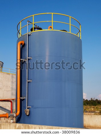 Blue oil storage tank with orange pipe and yellow rail on top.