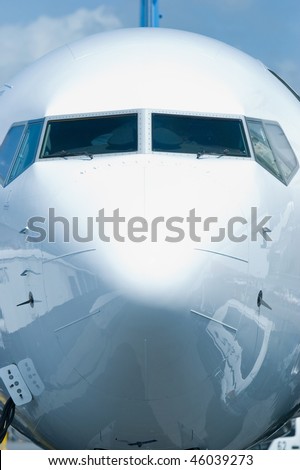 Front view of white passenger airplane with ground equipment reflected in the hull.