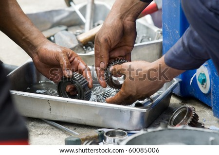 Hands of two car mechanics cleaning gearbox parts in petrol.