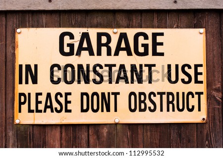a sign with the words Garage in constant use please do not obstruct requesting that vehicle drivers do not park blocking the entrance and exit to a garage