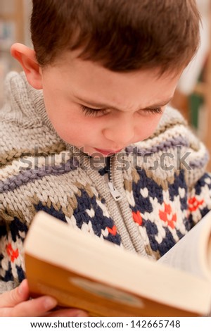 Little boy reading a paperback novel in an outside library.  The focus of the image is on the child intently reading, thereby blurring any text or titles to avod copyright issues.