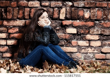 Lonely teenage girl sitting on the ground,a sad expression, leaning on an old brick wall.