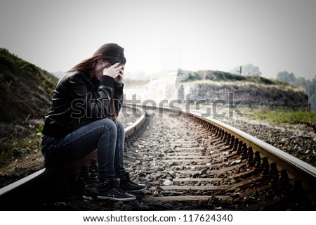 Depressed and lonely teenage girl with hands over her face sitting on the railroad