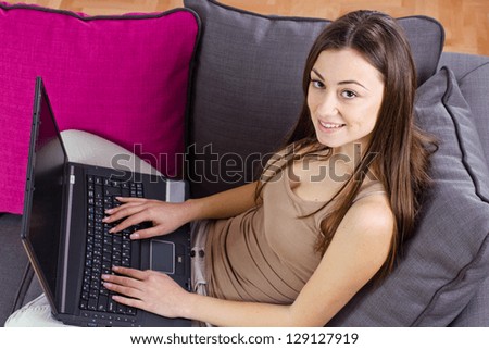 Happy teenage girl relax on sofa using laptop at home.