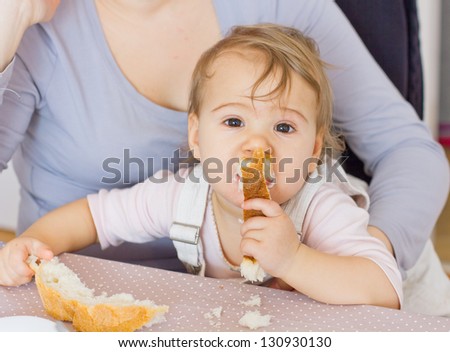 Funny cute baby eating bread and looking at camera.