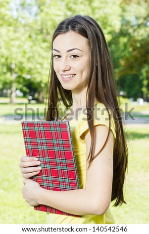 Portrait of happy female student with book in the park..