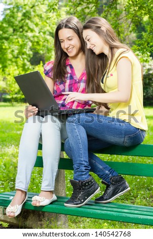 Two smiling female students using laptop in nature.