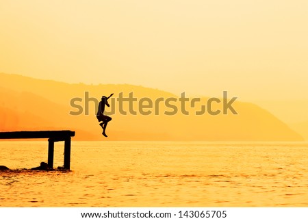 Silhouette of kids jumping from river dock, at sunset.