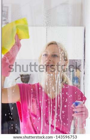 Housewife with protective glove washing the window glass.