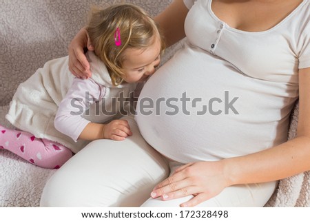 Happy child kissing belly of pregnant women.