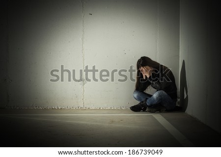 Depressed teenage girl with hands over face sitting in the corner.