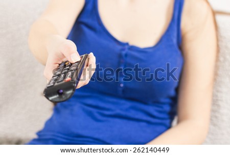 Close-up of unrecognizable woman with remote control change channels on TV.