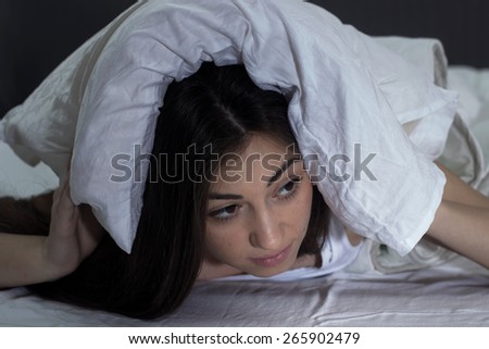 Worried Young Woman covered her head with pillow. Sleepless caucasian female.