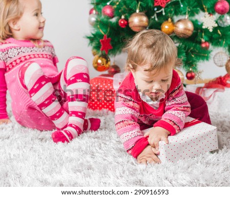 Charming happy children open Christmas presents on the floor and tree with New Year decoration at home.