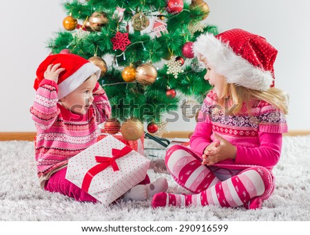 Happy children open Christmas presents on the floor and tree with New Year decoration at home.